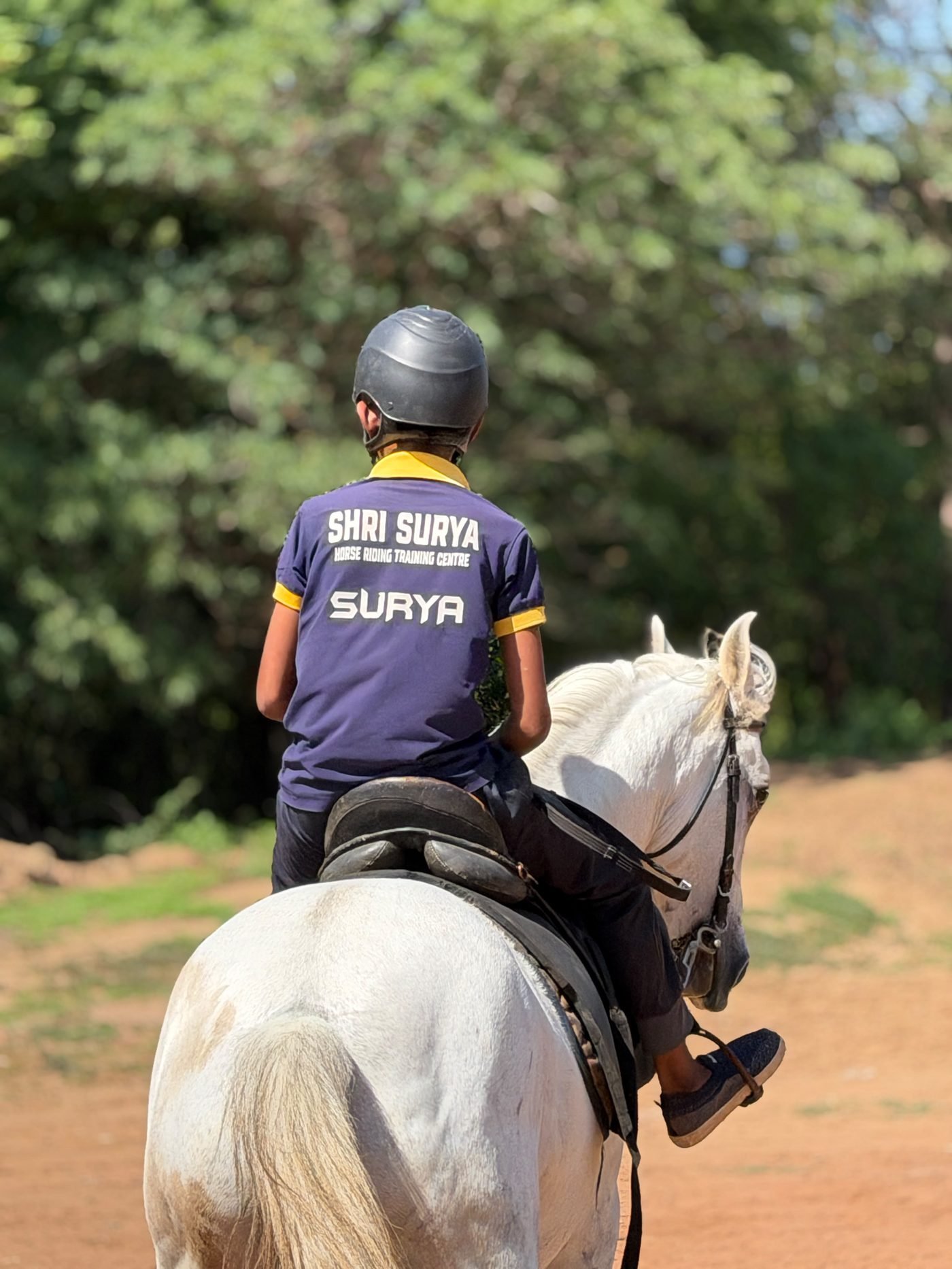 Young rider in Shri Surya Horse Riding Training Centre jersey riding a grey horse